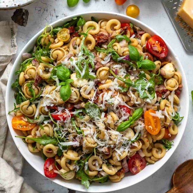 Gesunder Pasta Rezept mit Tomaten, süße, rote Zwiebeln, Basilikum, Rucola, sonnengetrocknete Tomaten, Kapern und Parmaschinken mit Balsamico-Olivenöl-Dressing.