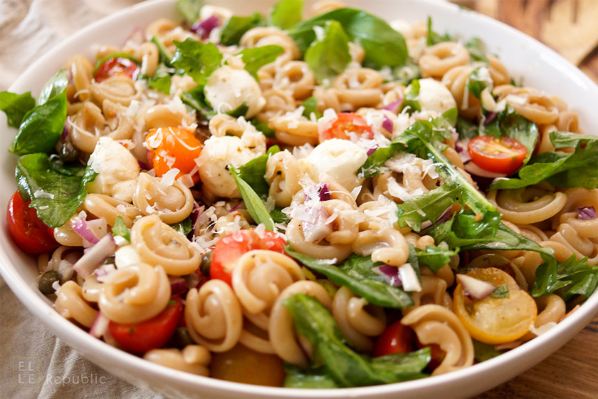 Sommer Pasta Rezept mit Tomaten, süße, rote Zwiebeln, Basilikum, Rucola, sonnengetrocknete Tomaten, Kapern und Parmaschinken mit Balsamico-Olivenöl-Dressing.