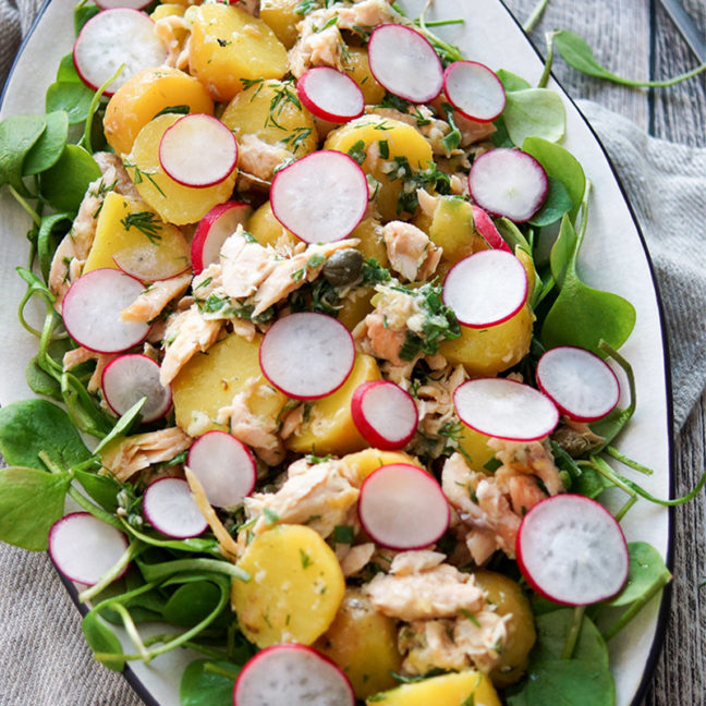 Kartoffelsalat mit Räuchersaibling Rezept. Jungen Kartoffeln, frischem Postelein (Portulak), Kapern, Frühlingszwiebel und Radieschen, mit einem Dressing aus Zitronensaft, Meerrettich, Dill und Olivenöl