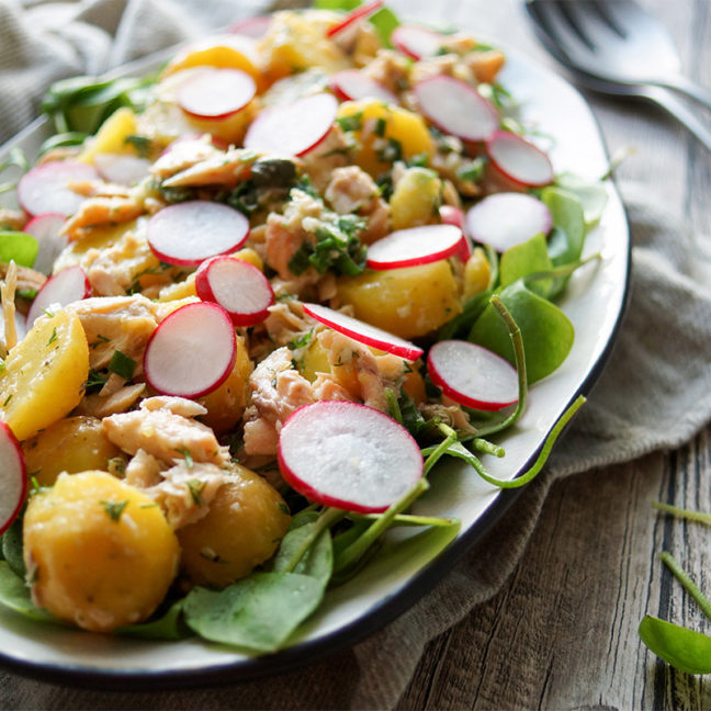 Kartoffelsalat mit Räuchersaibling Rezept. Jungen Kartoffeln, frischem Postelein (Portulak), Kapern, Frühlingszwiebel und Radieschen, mit einem Dressing aus Zitronensaft, Meerrettich, Dill und Olivenöl