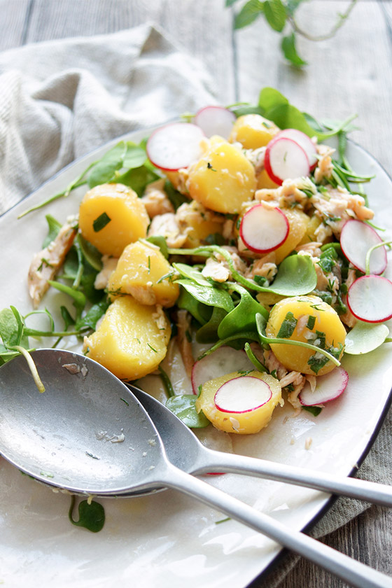 Kartoffelsalat mit Räuchersaibling Rezept. Jungen Kartoffeln, frischem Postelein (Portulak), Kapern, Frühlingszwiebel und Radieschen, mit einem Dressing aus Zitronensaft, Meerrettich, Dill und Olivenöl