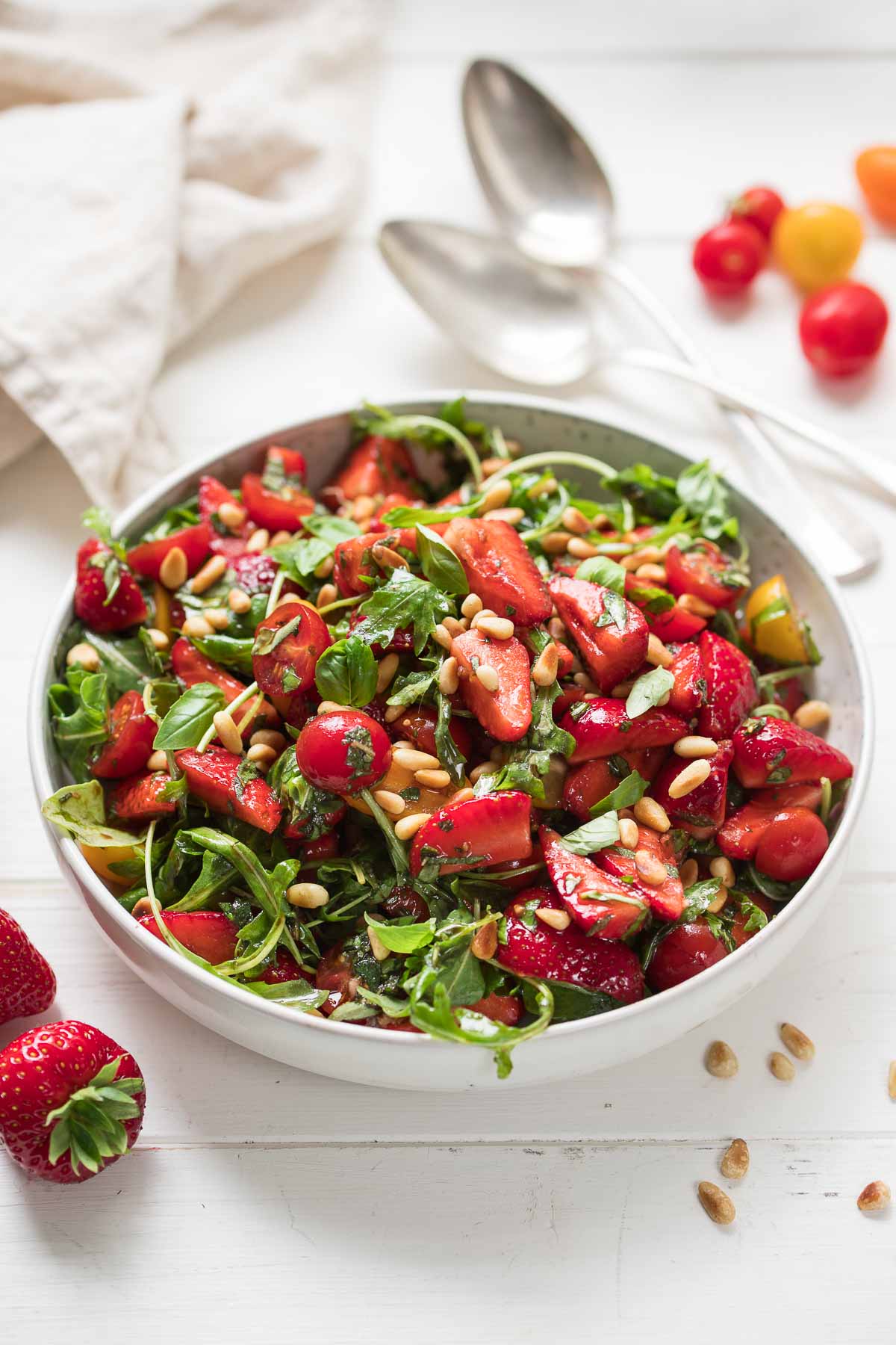 Salat mit Erdbeeren, Tomaten, Rucola, Minze und Basilikum im Schüssel mit Besteck