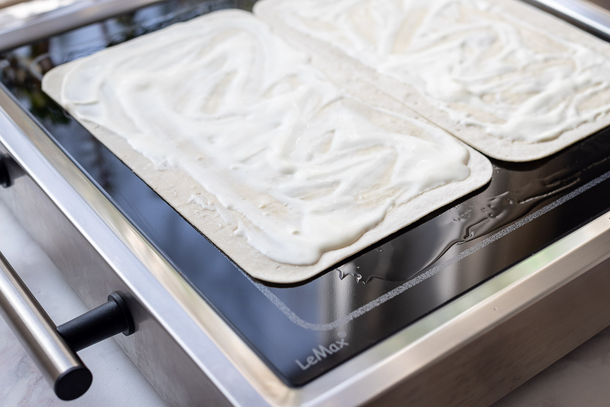 Tarte flambée bases with crème fraîche on a LeMax grill