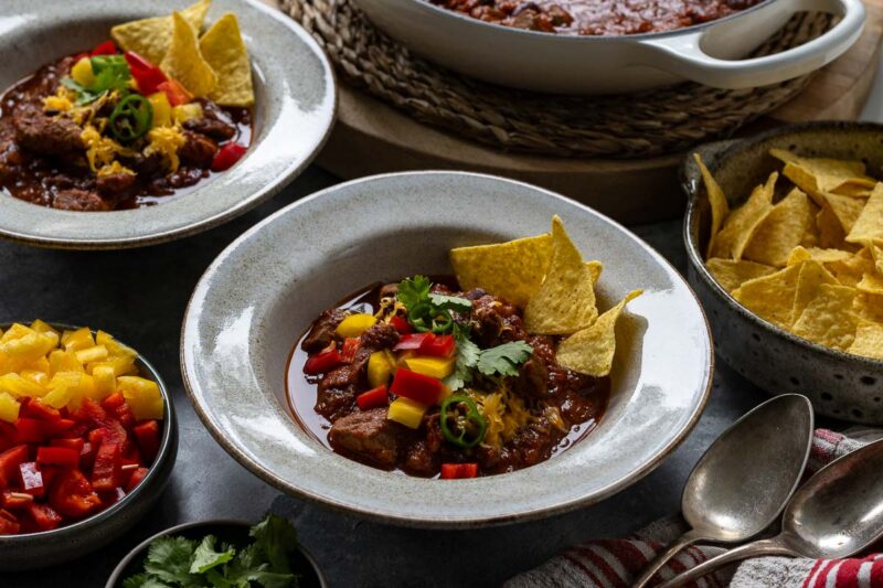 Chilli con Carne (Chunky Stew-Style Chili Recipe) served with diced paprika, tortilla chips, cilantro and cheddar cheese