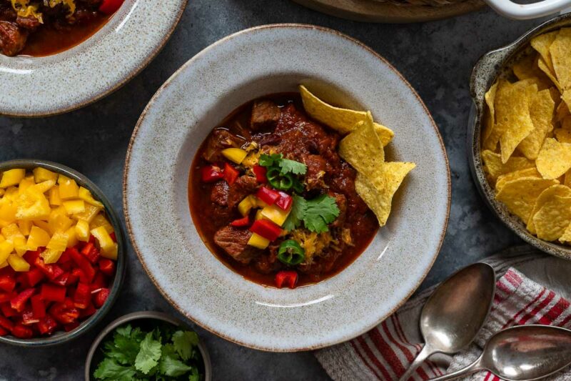 Chili con Carne mit Rindfleisch Rezept serviert mit Paprika, Cheddar-Käse und Tortilla Chips