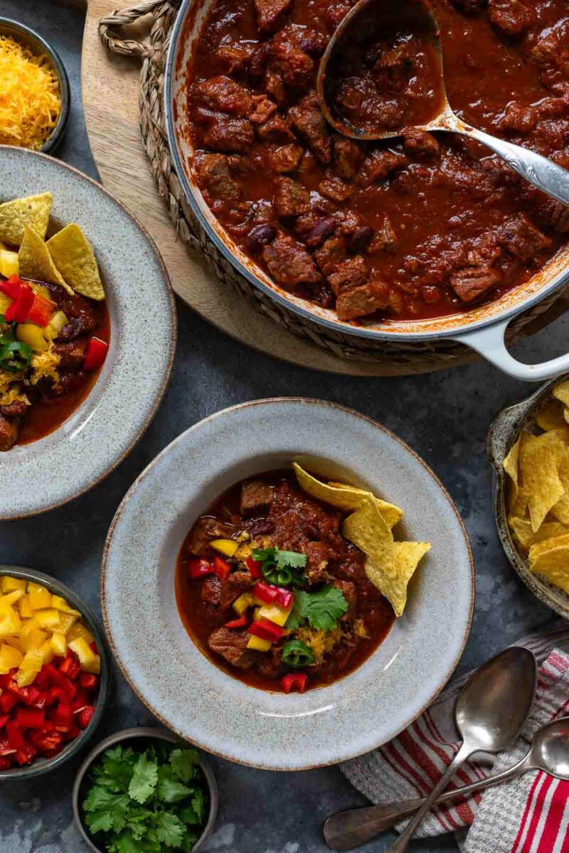 Chilli con Carne (Chunky Stew-Style Chili Recipe) served with diced paprika, tortilla chips, cilantro and cheddar cheese