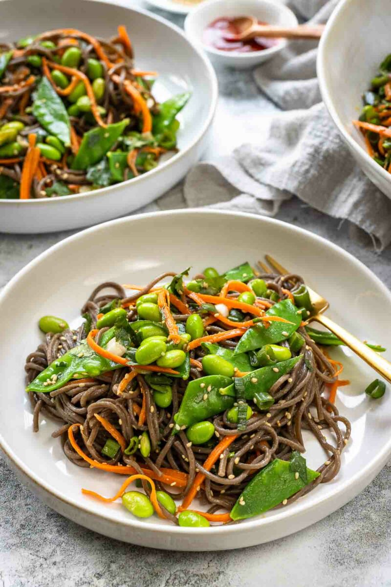 Miso Soba Noodle Salad with sugar snap peas, edamame, julienned carrots, green onion and miso dressing served into bowls (close-up)