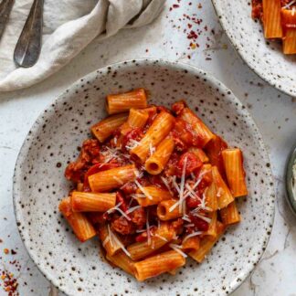 Rezept für Pasta mit Salsiccia in pikante Tomaten-Paprika-Sauce, garniert mit Parmesan angerichtet in einer Schüssel.