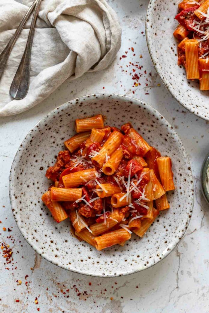 Rezept für Pasta mit Salsiccia in pikante Tomaten-Paprika-Sauce, garniert mit Parmesan angerichtet in einer Schüssel.