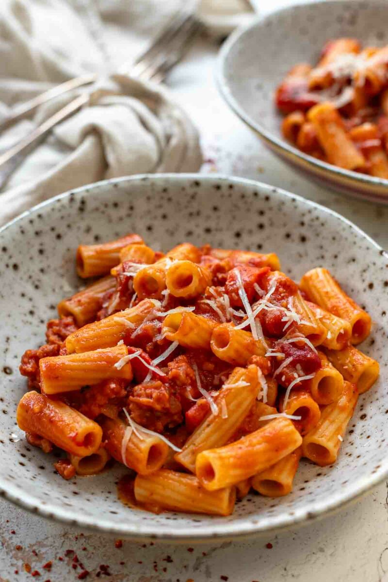 Servierte Pasta mit Salsiccia Rezept in pikante Tomaten-Paprika-Sauce, garniert mit Parmesan angerichtet in einer Schüssel.